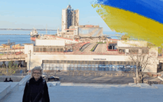 Beate Müller-Gemmeke geht eine breite Treppe hinauf. Im Hintergrund ist der Hafen von Odessa mit Containerschiffen und ein schwer beschädigtes Hochhaus zu sehen.