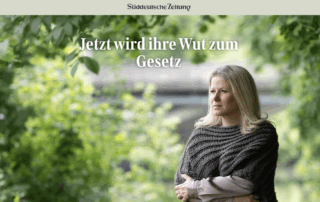 Titelbild der Süddeutschen Zeitung mit der Überschrift: „Jetzt wird ihre Wut zum Gesetz“. Im Vordergrund steht eine blonde Frau mit ernstem Blick, in dunklem Strickponcho und hellbluser Bluse, die Arme verschränkt. Im Hintergrund unscharf ein Fluss und grüne Bäume.