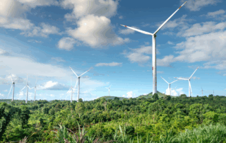 Mehrere moderne Windräder stehen inmitten grüner Hügellandschaft unter blauem Himmel mit einigen Wolken. Das Bild symbolisiert die Energiewende in Uruguay mit starkem Fokus auf Windkraft.