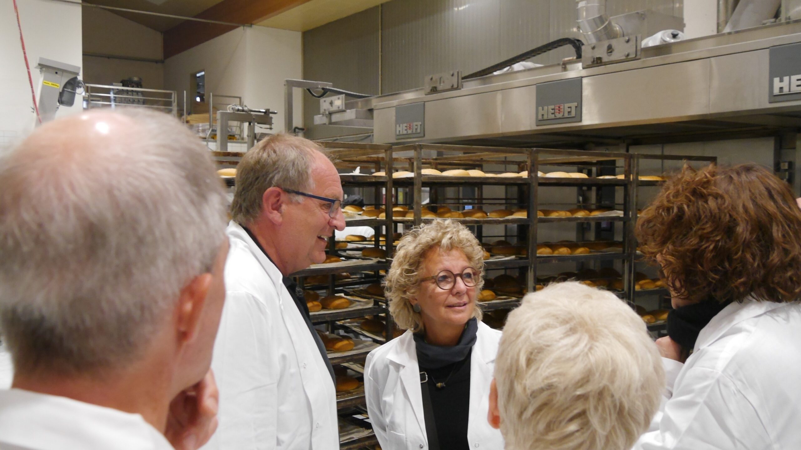 Beate Müller-Gemmeke im Gespräch mit dem Bäckermeister bei BeckaBeck – im Hintergrund die Backstube mit frischen Brötchen auf Blechen.