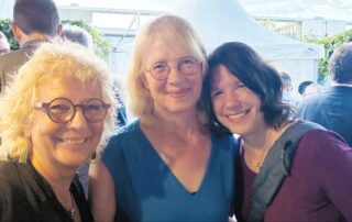 Beate Müller-Gemmeke mit Tabea Rößner (ehemalige MdB, Bündnis 90/Die Grünen) und Linda Heitmann (MdB, Bündnis 90/Die Grünen) beim Sommerfest der Deutschen Parlamentarischen Gesellschaft. Alle drei lächeln in die Kamera, im Hintergrund ein weißes Zelt.
