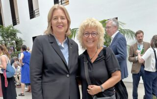 Beate Müller-Gemmeke zusammen mit Bärbel Bas, der neuen Bundesministerin für Arbeit und Soziales, beim Hoffest des BMAS. Beide stehen in einem modernen Innenhof und lächeln in die Kamera.