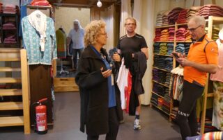 Beate Müller-Gemmeke im Laden von FLOMAX im Gespräch mit mehreren Personen. Um sie herum bunte, nachhaltig produzierte Strickkleidung.