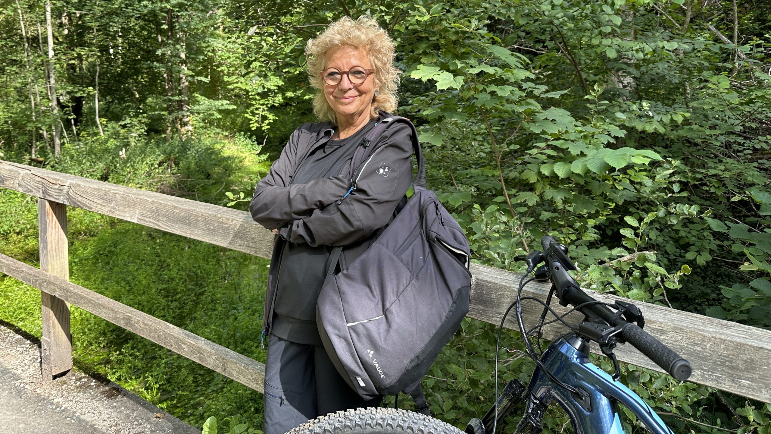 Beate Müller-Gemmeke lehnt auf einer Holzbrücke im Grünen neben ihrem Fahrrad während ihrer alljährlichen Albtour und lächelt in die Kamera.