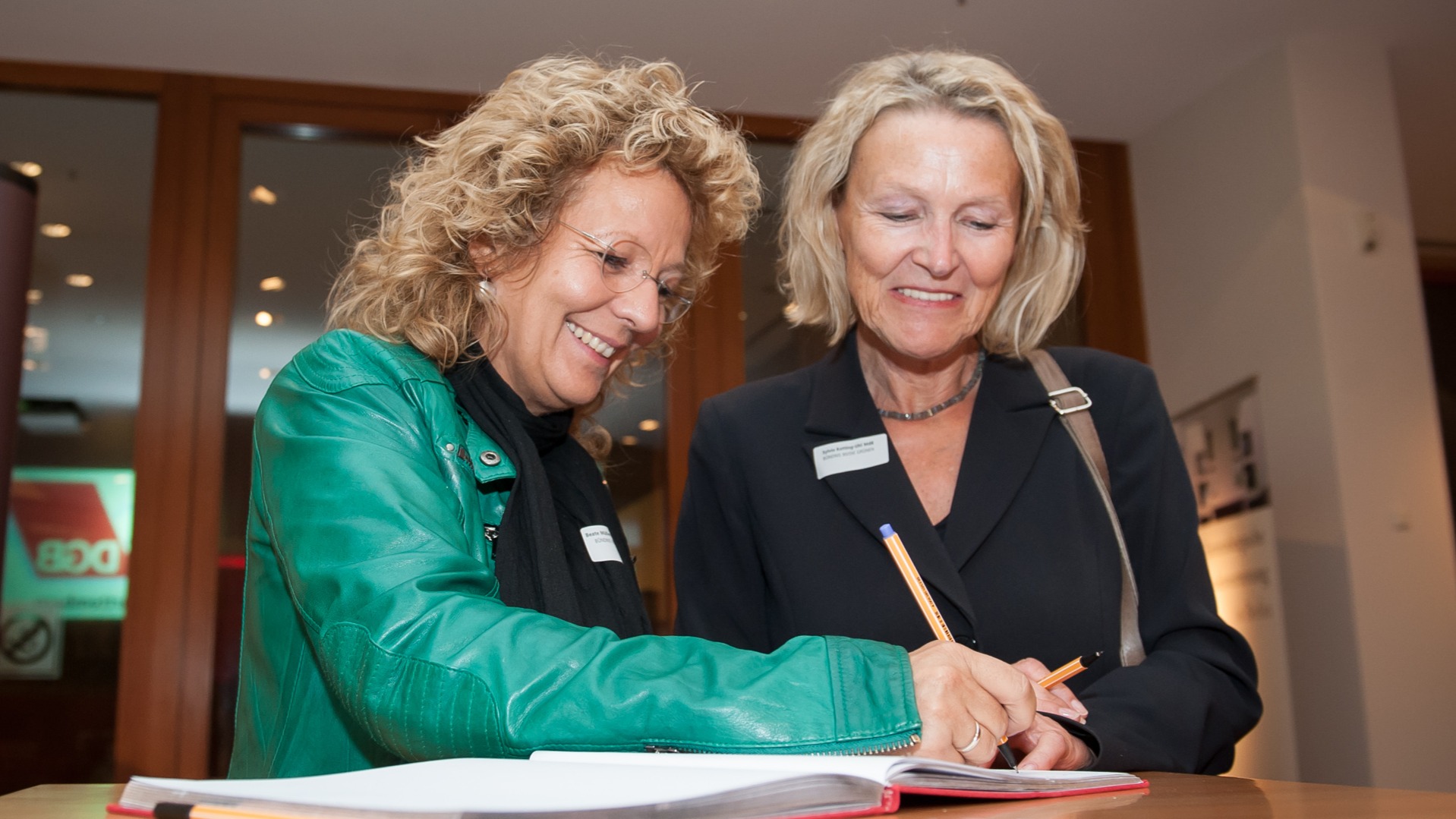 Beate Müller-Gemmeke und Sylvia Kotting-Uhl tragen sich gemeinsam in ein Gästebuch ein und lachen dabei herzlich.