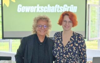Beate Müller-Gemmeke mit Sarah Gonschorek, die neu gewählten Sprecherinnen von GewerkschaftsGrün - vor der Leinwand mit dem Logo von GewerkschaftsGrün.