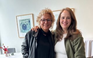 Beate Müller-Gemmeke und Ricarda Lang stehen nebeneinander, lachen in die Kamera und haben die Arme umeinander gelegt. Beate trägt eine schwarze Lederjacke, Ricarda ein weißes Kleid mit olivgrüner Jacke.