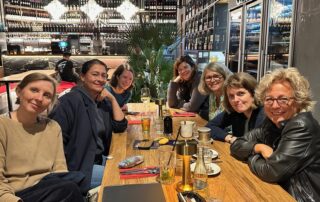 Gruppenfoto am Restauranttisch: Beate Müller-Gemmeke sitzt mit sechs Frauen an einem langen Tisch, Getränke und Gläser stehen vor ihnen. Alle lächeln in die Kamera, die Atmosphäre ist herzlich und lebendig.