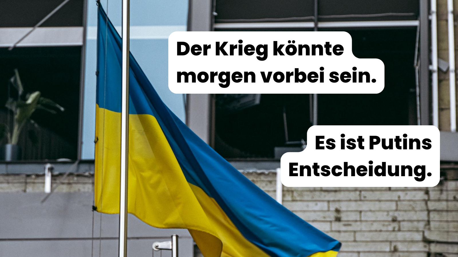 Ukrainische Flagge weht vor einem beschädigten Gebäude mit eingeschlagenen Fenstern. Auf dem Bild steht der Text: „Der Krieg könnte morgen vorbei sein. Es ist Putins Entscheidung.“ Die Aufnahme symbolisiert Zerstörung und Verantwortung für den Krieg in der Ukraine.