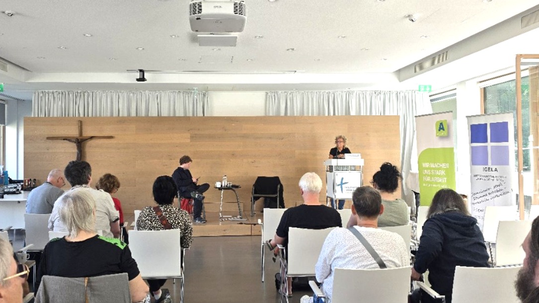 Beate Müller-Gemmeke spricht am Rednerpult vor dem Publikum der Arbeitslosentagung. Im Hintergrund sind Roll-ups der Veranstalter zu sehen, vor ihr sitzen aufmerksam zuhörende Teilnehmende in hellen Stuhlreihen.