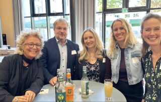 Gruppenfoto am Stehtisch beim Fachtag in Berlin: Beate Müller-Gemmeke mit vier Teilnehmenden, alle lächeln in die Kamera. Auf dem Tisch stehen mehrere Flaschen mit Getränken.