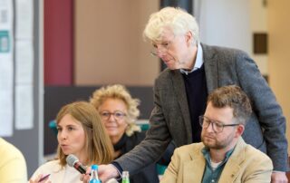 Diskussionsszene beim Fachtag in Berlin: Eine junge Frau spricht ins Mikrofon, während ein älterer Mann das Mikro hält. Beate Müller-Gemmeke sitzt im Hintergrund und hört aufmerksam zu.