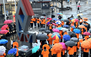 Blick auf den Reutlinger Marktplatz: Viele Menschen in orangefarbenen T-Shirts stehen dicht gedrängt mit bunten Regenschirmen. In der Mitte ragt die Skulptur am Marktplatz auf. Beate Müller-Gemmeke befindet sich unter den Teilnehmenden. Die Gruppe setzt gemeinsam ein sichtbares Zeichen gegen Gewalt an Frauen.