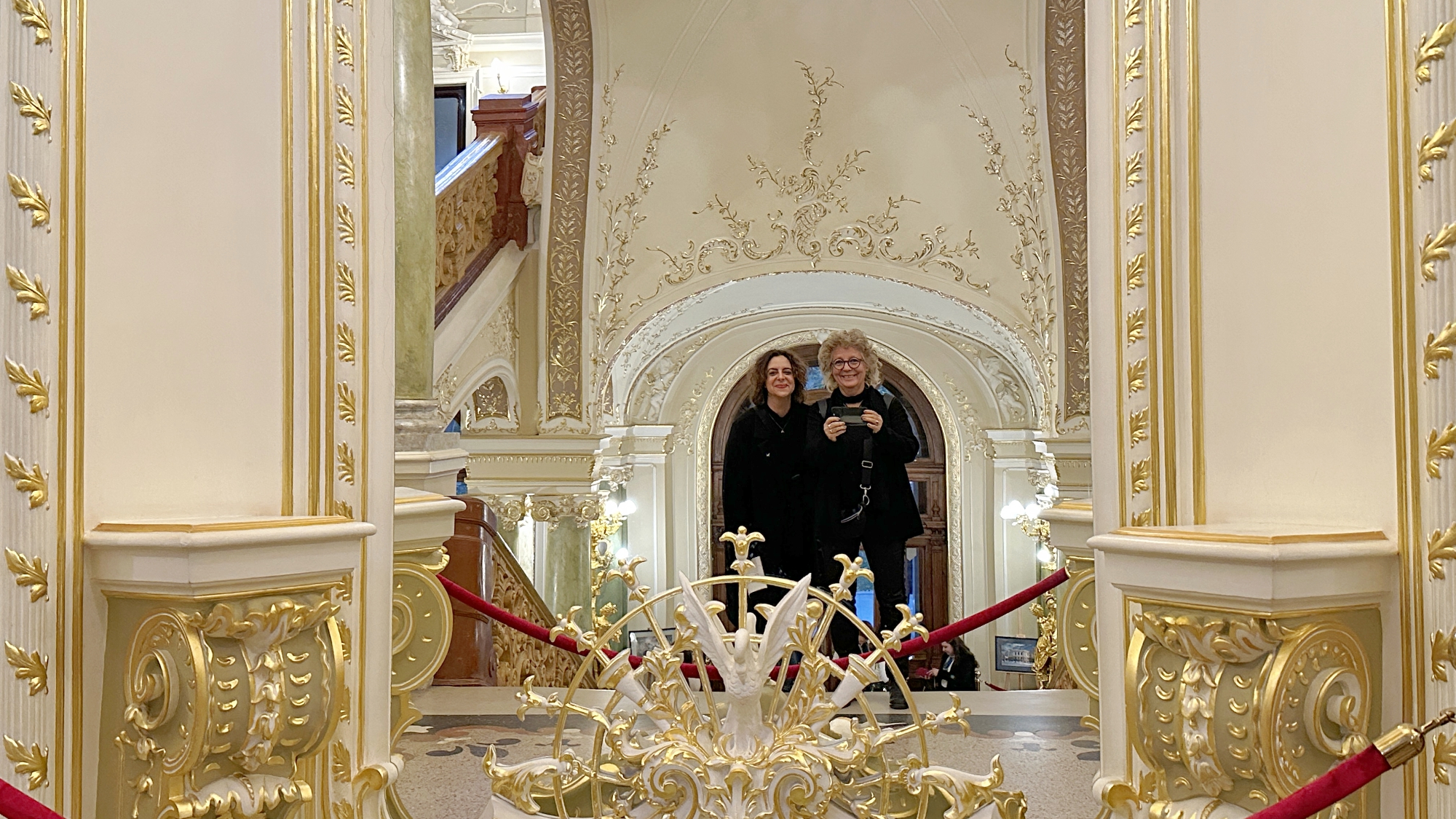 Beate Müller-Gemmeke und eine Begleiterin im prunkvollen Foyer der Oper Odessa – goldene Verzierungen, Spiegel und festliche Atmosphäre.