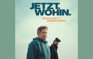 Filmplakat zu JETZT. WOHIN. Meine Reise mit Robert Habeck. Robert Habeck und Regisseur Lars Jessen stehen am Wasser, Blick in die Kamera. Der Himmel ist leicht bewölkt, der Hintergrund zeigt See und Uferlinie. Der Titel des Films steht groß oben im Bild.