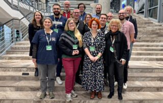 Beate Müller-Gemmeke steht mit ihrer Co-Sprecherin Sarah Gonschorek und einer Gruppe von GewerkschaftsGrünen auf einer Treppe im Kongresszentrum der BDK in Hannover. Rund 15 Menschen lächeln in die Kamera, viele mit Delegierten-Badges um den Hals. Die Stimmung wirkt offen und zugewandt.