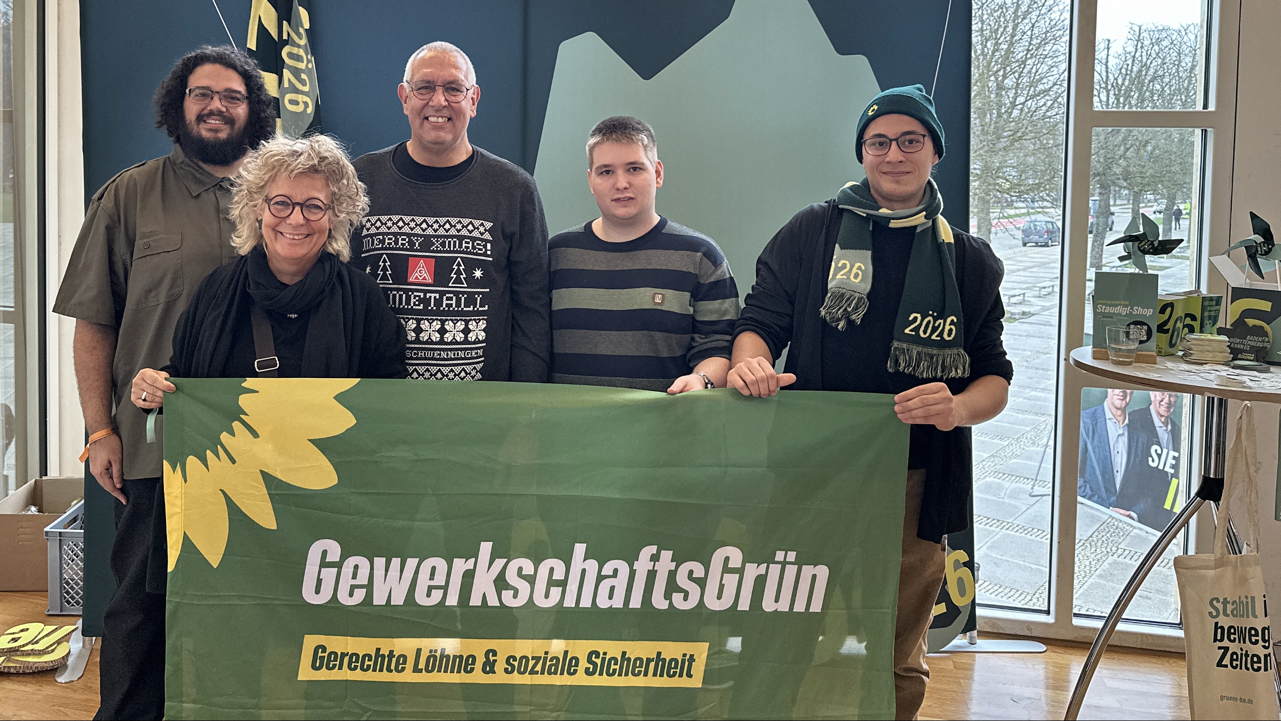 Beate Müller-Gemmeke steht mit Mitgliedern von GewerkschaftsGrün vor einer grünen Kulisse, gemeinsam halten sie ein Banner mit der Aufschrift GewerkschaftsGrün – Gerechte Löhne und soziale Sicherheit.