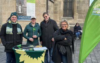 Vier Personen stehen an einem Grünen-Infostand in Reutlingen. Ganz links steht Thomas Poreski, Landtagsabgeordneter und Kandidat für die Landtagswahl 2026. Rechts steht Beate Müller-Gemmeke. Auf dem Tisch liegen Informationsmaterialien, im Hintergrund ist eine Kirche zu sehen.