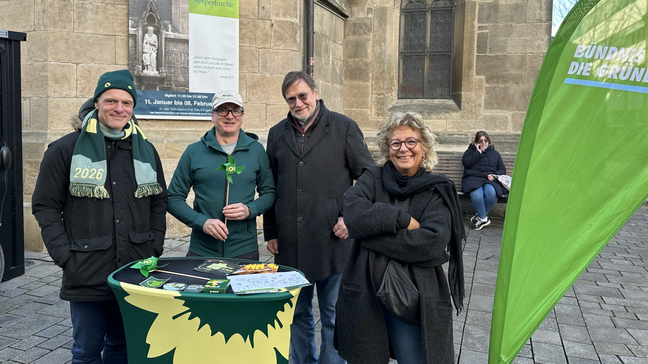 Vier Personen stehen an einem Grünen-Infostand in Reutlingen. Ganz links steht Thomas Poreski, Landtagsabgeordneter und Kandidat für die Landtagswahl 2026. Rechts steht Beate Müller-Gemmeke. Auf dem Tisch liegen Informationsmaterialien, im Hintergrund ist eine Kirche zu sehen.