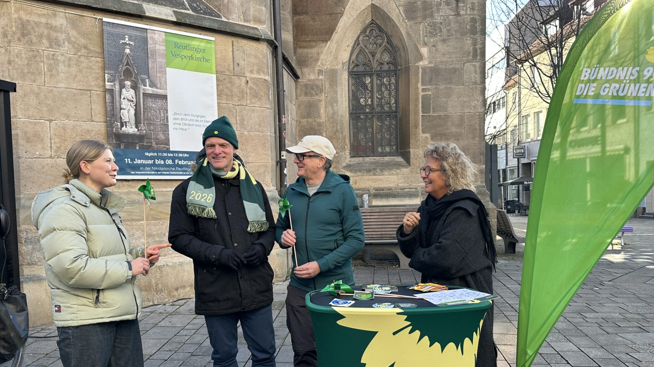 Infostand von Bündnis 90/Die Grünen in Reutlingen. Ganz links steht Thomas Poreski. Beate Müller-Gemmeke steht am Stehtisch im Gespräch mit weiteren Beteiligten. Rechts ist ein grünes Beachflag von Bündnis 90/Die Grünen zu sehen.