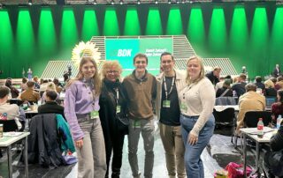 Beate Müller-Gemmeke steht mit vier jungen Menschen aus dem Reutlinger Team vor der großen grünen BDK-Bühne. Alle tragen Delegierten-Badges und lächeln in die Kamera. Der Saal ist voll, im Hintergrund ist das Veranstaltungslogo „Damit Zukunft wieder Zukunft hat“ zu sehen.