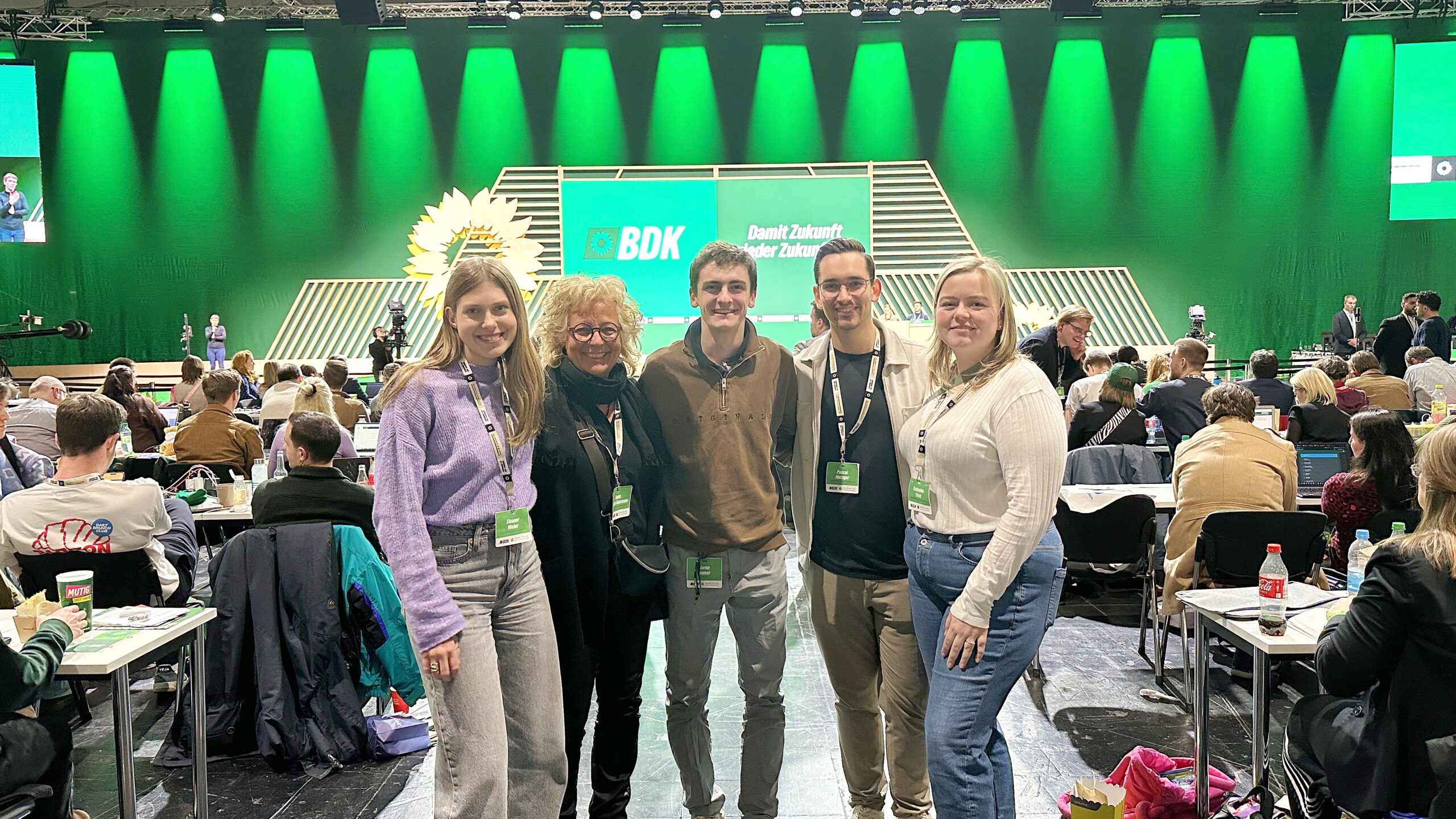 Beate Müller-Gemmeke steht mit vier jungen Menschen aus dem Reutlinger Team vor der großen grünen BDK-Bühne. Alle tragen Delegierten-Badges und lächeln in die Kamera. Der Saal ist voll, im Hintergrund ist das Veranstaltungslogo „Damit Zukunft wieder Zukunft hat“ zu sehen.