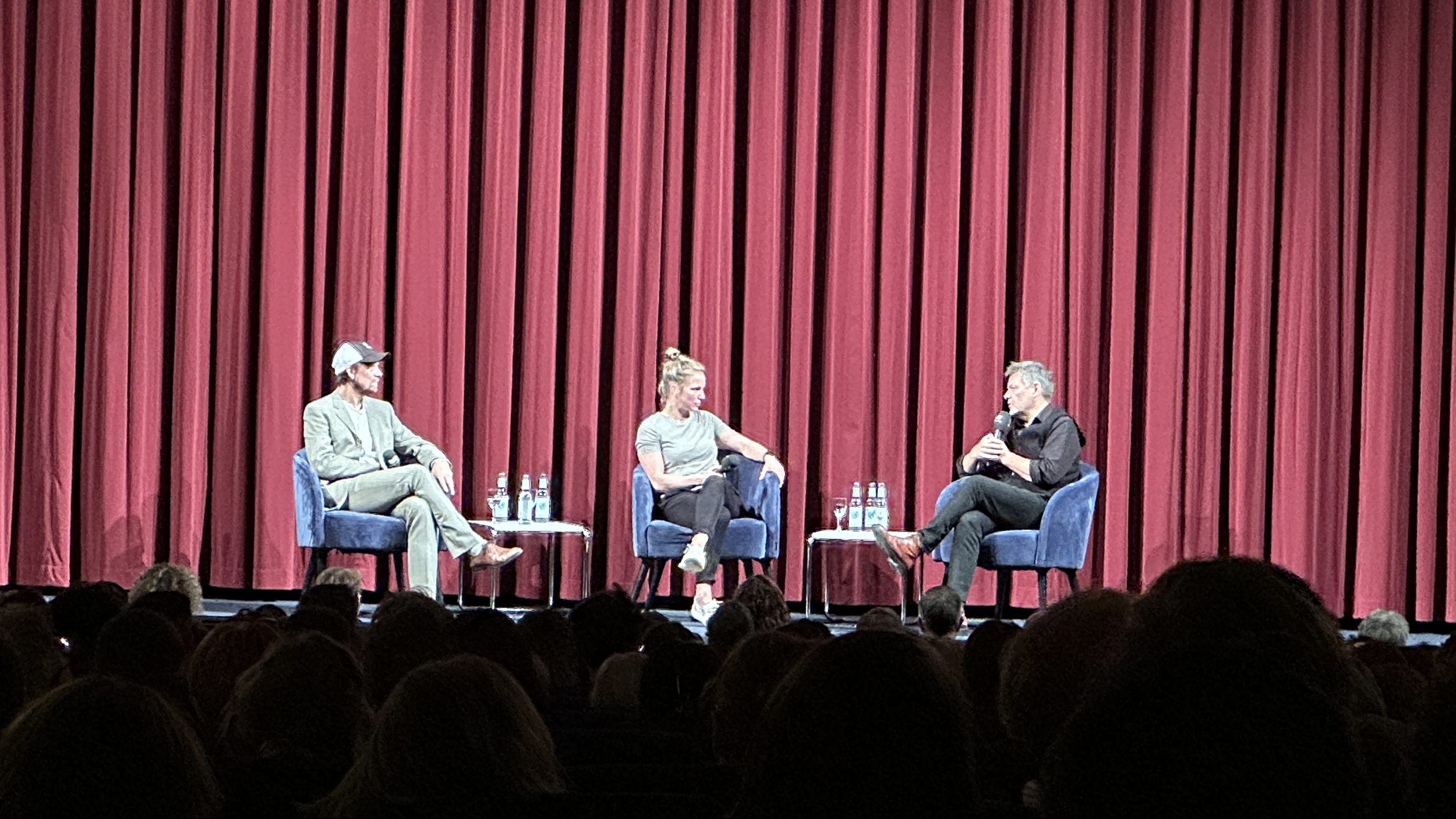 Auf der Kinobühne sitzen drei Personen auf Stühlen vor einem roten Vorhang: Lars Jessen, eine Moderatorin und Robert Habeck. Sie führen ein Gespräch nach der Filmvorführung. Auf kleinen Tischen stehen Wasserflaschen. Das Publikum schaut von unten auf die Bühne.