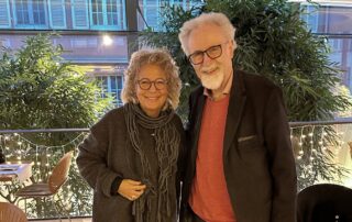 Beate Müller-Gemmeke und Prof. Dr. Wolfgang Däubler stehen nebeneinander in einem hellen Innenraum mit Pflanzen im Hintergrund. Beide lächeln in die Kamera; es ist eine ruhige, vertraute, persönliche Atmosphäre.