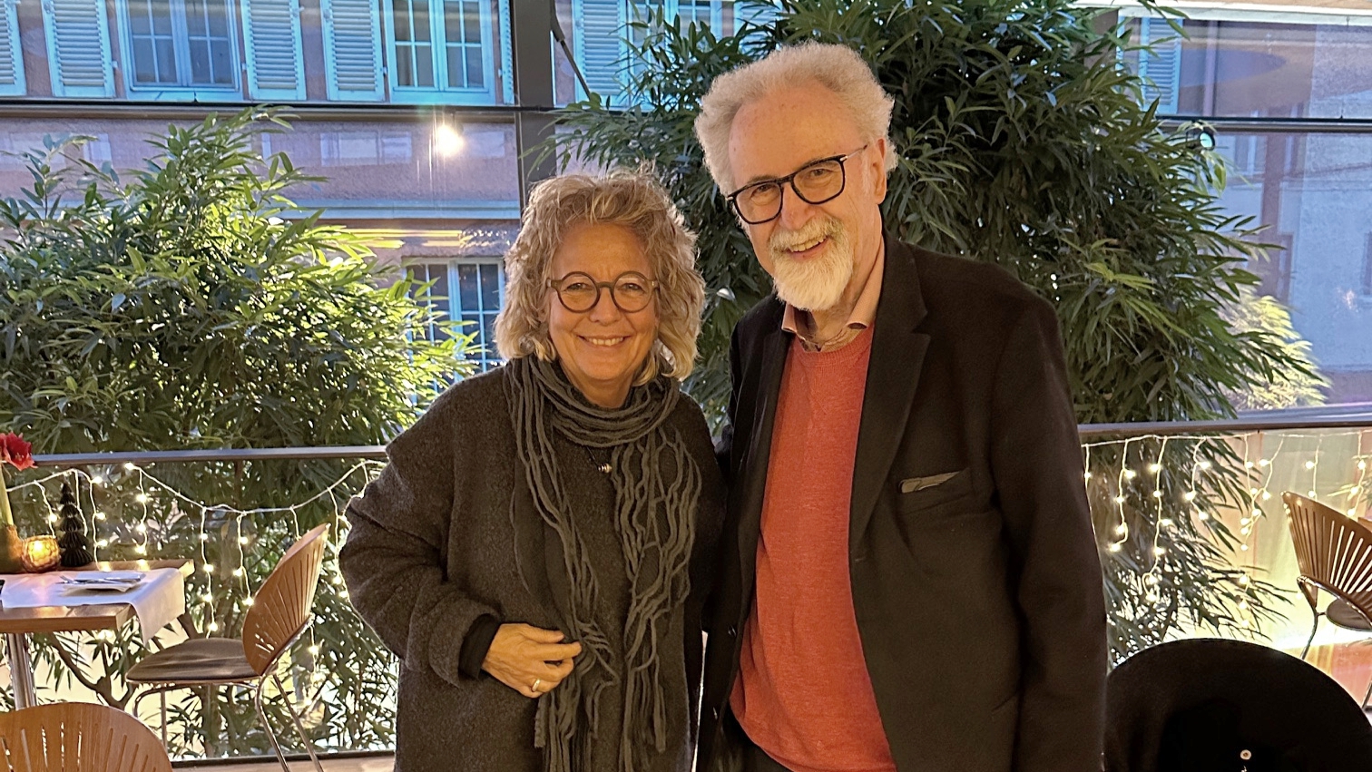 Beate Müller-Gemmeke und Prof. Dr. Wolfgang Däubler stehen nebeneinander in einem hellen Innenraum mit Pflanzen im Hintergrund. Beide lächeln in die Kamera; es ist eine ruhige, vertraute, persönliche Atmosphäre.