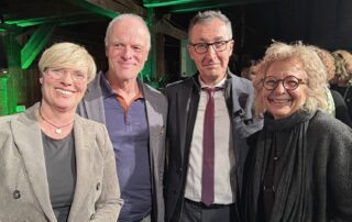 Vier Personen stehen eng nebeneinander in der historischen Festkelter in Metzingen und lächeln in die Kamera. In der Mitte steht Cem Özdemir, links und rechts von ihm stehen Cindy Holmberg, Thomas Poreski und Beate Müller-Gemmeke. Im Hintergrund sind Holzbalken der Festkelter zu sehen, die grün beleuchtet sind. Die Stimmung wirkt offen und herzlich.