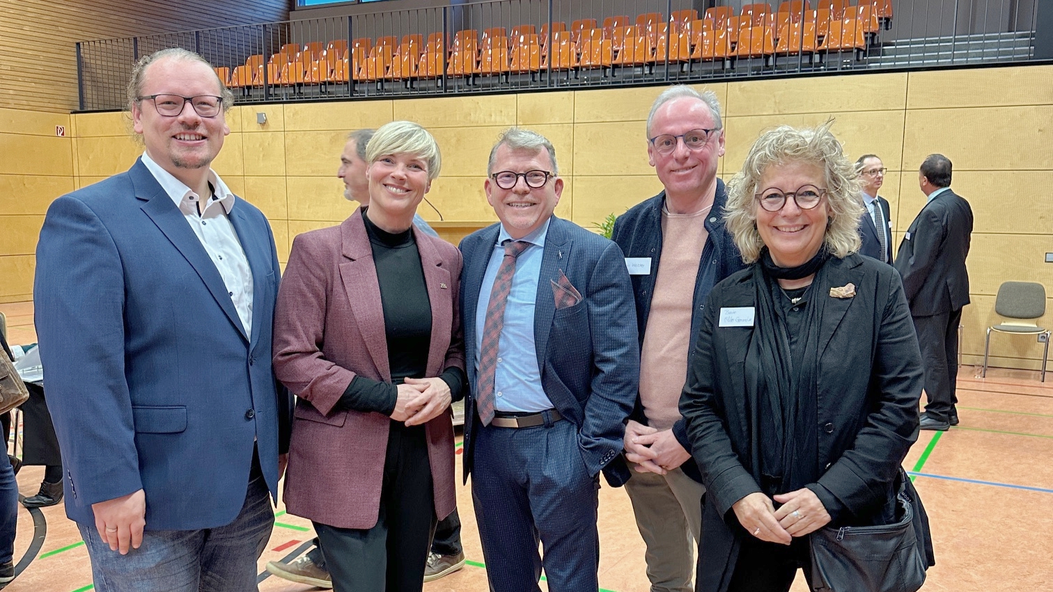 Alt-Text: Gruppenfoto beim Neujahrsempfang in Münsingen: In der Mitte Bürgermeister Mike Münzing. Links von ihm Cindy Holmberg, Landtagsabgeordnete und Kandidatin, sowie Beate Müller-Gemmeke. Daneben zwei grüne Gemeinderäte aus Münsingen. Alle stehen in einer Sporthalle und lächeln in die Kamera.
