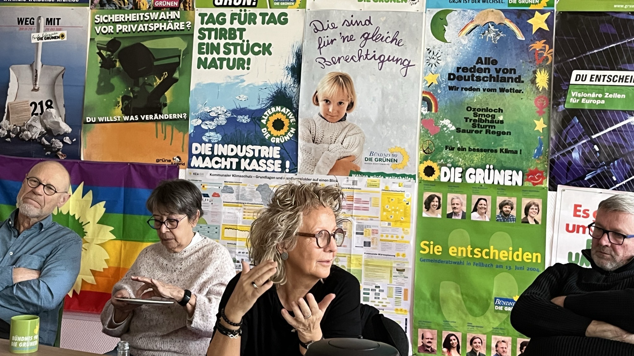 Diskussionsrunde der Grünen in Waiblingen zum Thema Bürgergeld und Grundsicherung. Beate Müller-Gemmeke spricht an einem Tisch, andere Teilnehmende hören aufmerksam zu. Im Hintergrund hängen historische Wahlplakate von Bündnis 90/Die Grünen.