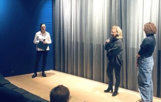 Nach der Filmvorführung beantwortet Beate Müller-Gemmeke und Lisa Weigert Fragen des Publikums; neben ihr steht eine Mitveranstalterin auf der Bühne vor einem Vorhang.
