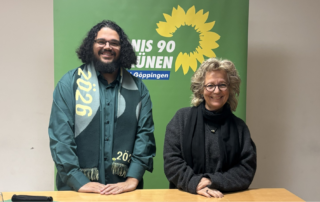 Beate Müller-Gemmeke und Landtagskandidat Julian Beier stehen vor einem grünen Banner von Bündnis 90/Die Grünen Göppingen und lächeln in die Kamera.