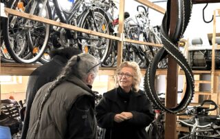 Beate Müller-Gemmeke im Gespräch mit Mitarbeitenden in der Fahrrad-Werkstatt Geislingen; im Hintergrund stehen zahlreiche reparierte Fahrräder in Regalen.