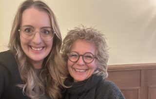 Beate Müller-Gemmeke und Fraktionsvorsitzende Katharina Dröge lächeln in die Kamera. Beide tragen dunkle Kleidung, im Hintergrund ein heller Innenraum. Aufnahme bei einem politischen Austausch in Berlin.