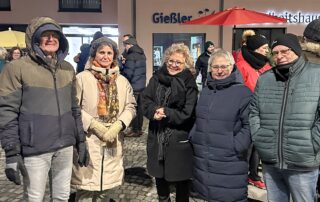 Mehrere Teilnehmende der Mahnwache stehen abends auf dem Marktplatz in Burladingen im Gespräch mit Beate Müller-Gemmeke. Sie tragen winterliche Kleidung, im Hintergrund sind weitere Menschen und Gebäude zu sehen. Die Gruppe steht dicht beieinander und zeigt Präsenz und Zusammenhalt bei der Mahnwache für Demokratie.