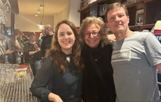 Ricarda Lang, Beate Müller-Gemmeke und der Kneipenwirt stehen gemeinsam hinter der Theke im Vis-à-Vis und lächeln in die Kamera. Im Hintergrund sind weitere Gäste und das Bar-Ambiente mit Gläsern und Zapfanlage zu sehen.