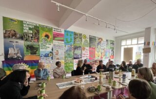 Große Diskussionsrunde der Grünen Waiblingen zum Thema Grundsicherung. Beate Müller-Gemmeke spricht mit den Teilnehmenden, Menschen unterschiedlichen Alters sitzen an einem Tisch und diskutieren. Der Raum ist mit Wahlplakaten von Bündnis 90/Die Grünen gestaltet.