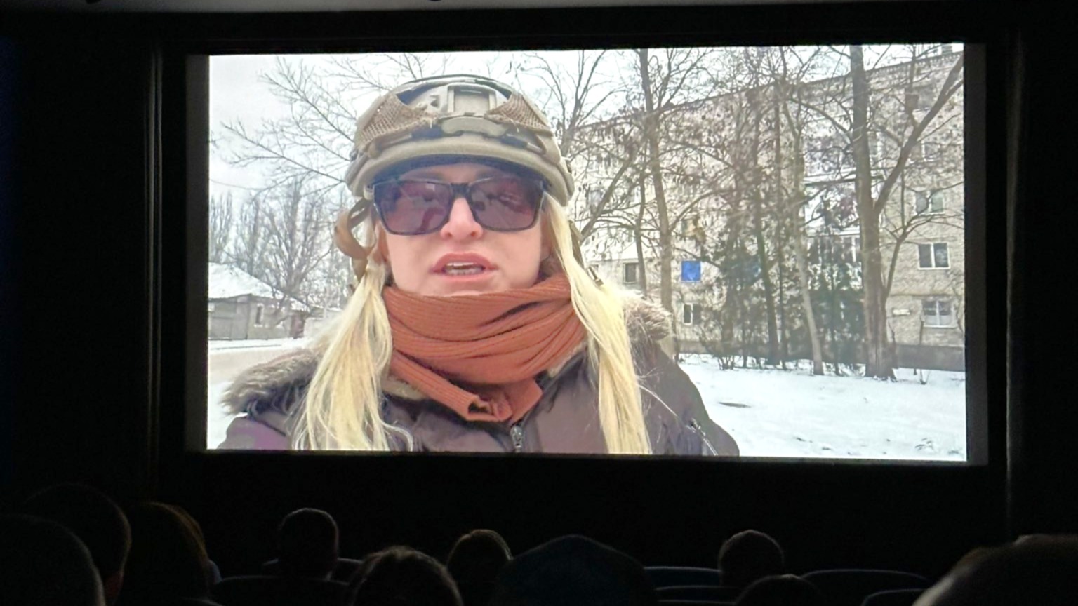 Filmszene im Kinosaal: Die Journalistin Zarina Zabrisky berichtet im Winter aus der ukrainischen Stadt Cherson; im Vordergrund sind die Silhouetten des Publikums zu erkennen.