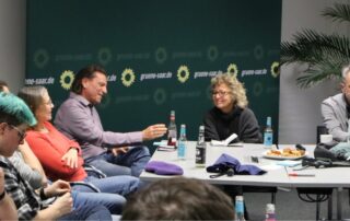Diskussionsrunde bei der Gründungsveranstaltung von GewerkschaftsGrün Saar. Beate Müller-Gemmeke und Volker Morbe sitzen gemeinsam am Tisch, hören zu und diskutieren mit den Teilnehmenden vor einem grünen Hintergrund mit Parteilogo.