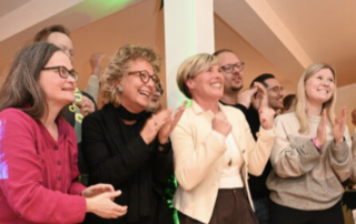 Beate Müller-Gemmeke steht neben Cindy Holmberg und weiteren Grünen bei der Wahlfete und verfolgt gemeinsam mit ihnen gespannt die ersten Wahlergebnisse.