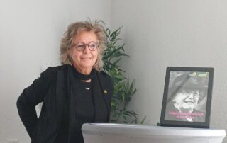 Beate Müller-Gemmeke steht an einem Rednerpult und spricht bei der Verleihung des Irmgard-Zecher-Preises. Neben ihr steht ein gerahmtes Porträt von Irmgard Zecher mit dem Hinweis auf die Auszeichnung für Bettina Noack.