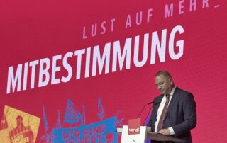 Frank Werneke, Bundesvorsitzender von ver.di, steht an einem Rednerpult auf einer Bühne. Hinter ihm ist eine große rote Leinwand mit der Aufschrift „Mitbestimmung“ und dem ver.di-Logo zu sehen.