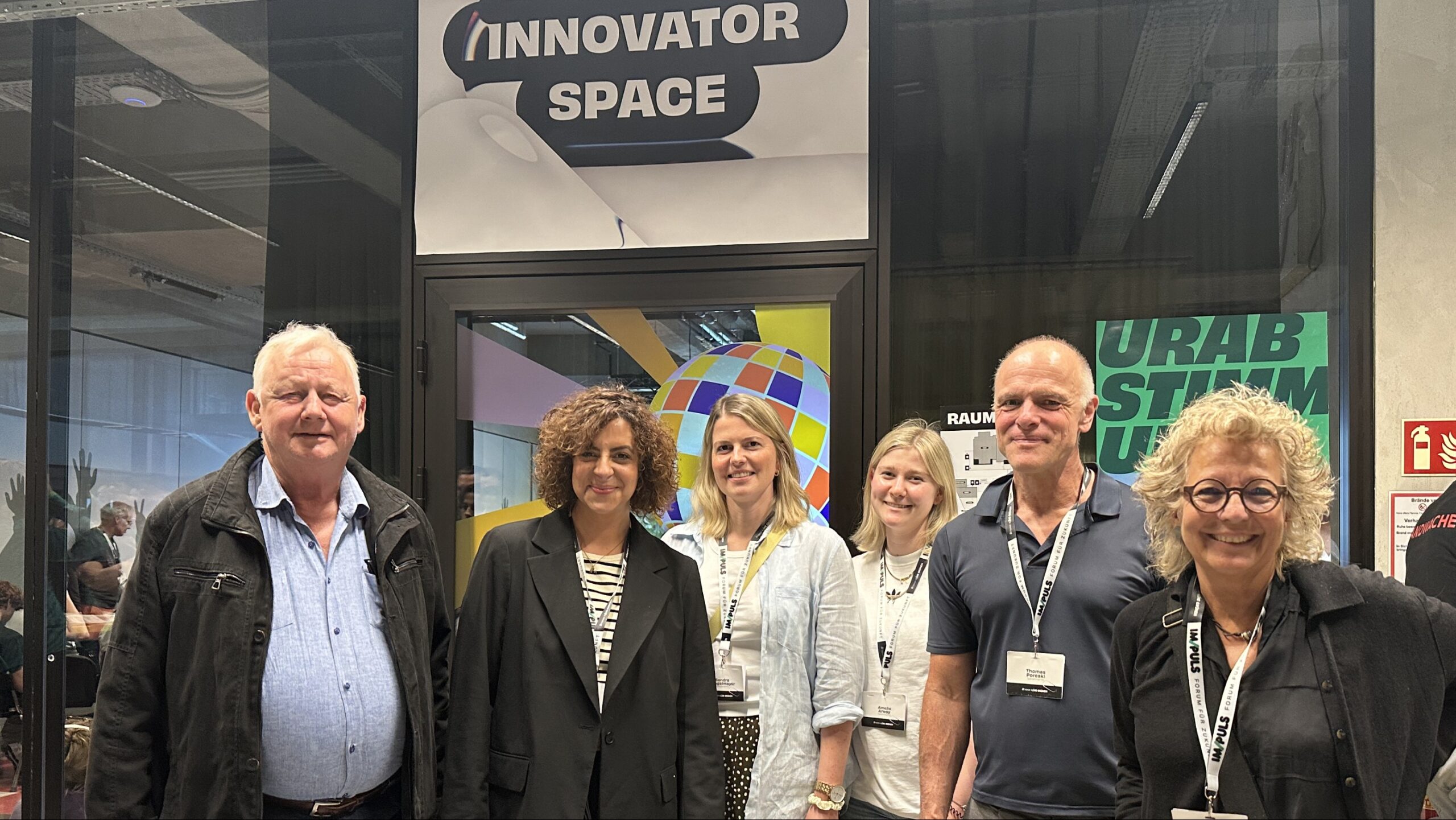 Beate Müller-Gemmeke mit Grünen aus dem Kreisverband Reutlingen vor dem Eingang des „Innovator Space“ beim IM/PULS-Forum. Die Gruppe steht für ein gemeinsames Erinnerungsfoto zusammen.