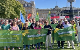 Größere Gruppe von GewerkschaftsGrün bei der Kundgebung auf dem Stuttgarter Schlossplatz. Die Teilnehmenden stehen hinter mehreren grünen Bannern und Fahnen, im Hintergrund sind der Schlossplatz, der Brunnen und zahlreiche weitere Demonstrierende zu sehen.