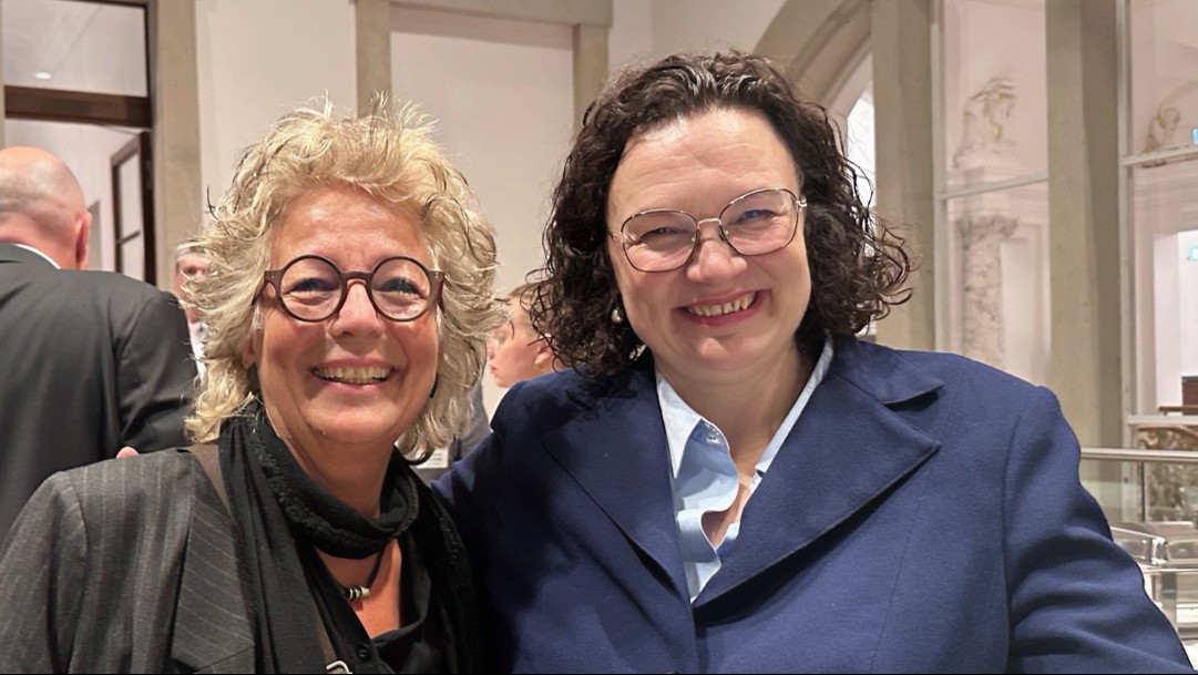 Andrea Nahles und Beate Müller-Gemmeke stehen beim BA-Empfang im Bundestag eng nebeneinander und lächeln in die Kamera. Andrea Nahles trägt einen dunkelblauen Blazer über einer hellblauen Bluse, Beate Müller-Gemmeke schwarze Kleidung.