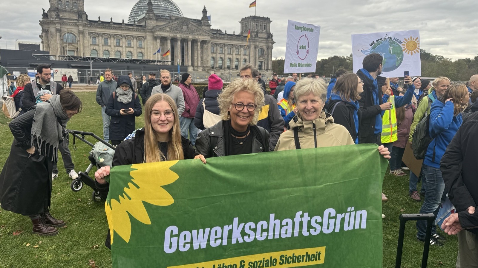 Beate Müller-Gemmeke steht mit Teilnehmenden der Jahrestagung von GewerkschaftsGrün bei der Demonstration für die Erneuerbaren auf der Reichstagswiese in Berlin. Sie halten gemeinsam ein großes GewerkschaftsGrün-Banner vor dem Reichstagsgebäude.