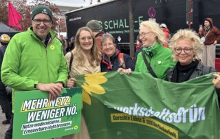 Katharina Dröge, Fraktionsvorsitzende der Grünen im Bundestag, Michael Kellner und Beate Müller-Gemmeke treffen sich bei der Demonstration für die Erneuerbaren auf der Reichstagswiese in Berlin. Gemeinsam stehen sie mit weiteren Teilnehmenden hinter einem GewerkschaftsGrün-Banner.
