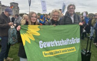 Beate Müller-Gemmeke steht mit Teilnehmenden der Jahrestagung von GewerkschaftsGrün bei der Demonstration für die Erneuerbaren in Berlin. Sie halten gemeinsam das GewerkschaftsGrün-Banner, während im Hintergrund weitere Demonstrierende zu sehen sind.